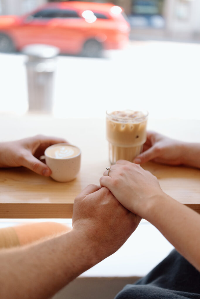 Engaged couple holding hands at a coffee shop for their engagement photos.