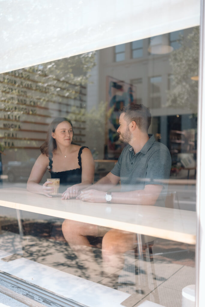 Couple talking through the window of a coffee shop for their engagement photos.